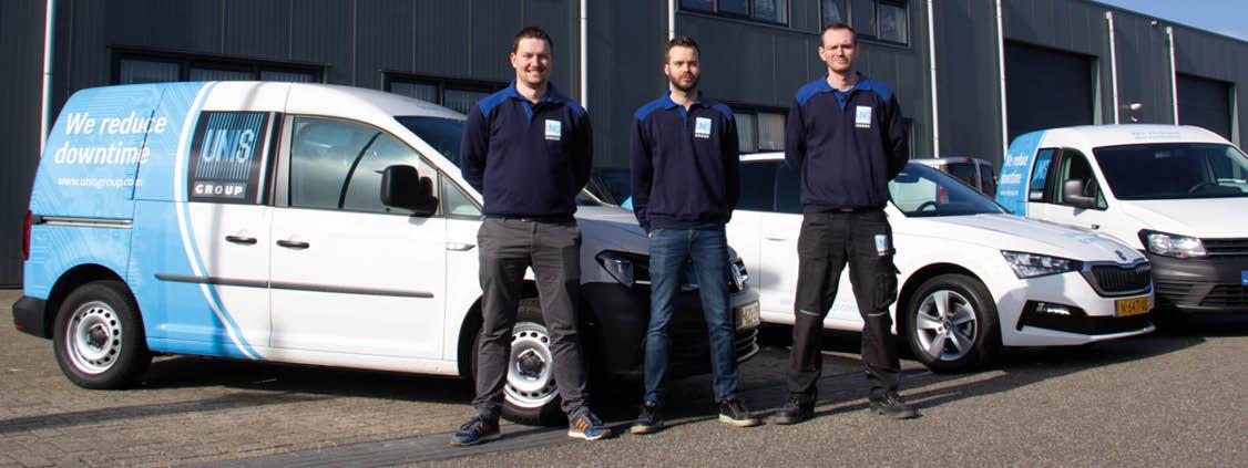 Three service technicians standing beside UNIS Group service vehicles outside a building.